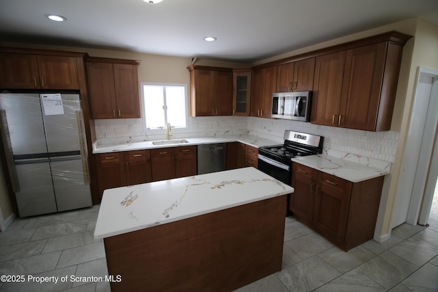 kitchen with stainless steel appliances, tasteful backsplash, a kitchen island, light stone counters, and sink