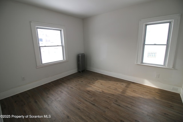 empty room featuring dark wood-type flooring, a wealth of natural light, and radiator