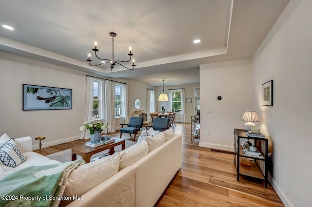 living room with a raised ceiling, light hardwood / wood-style floors, and an inviting chandelier