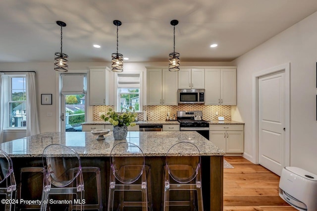 kitchen with white cabinetry, light stone countertops, a center island, decorative light fixtures, and appliances with stainless steel finishes