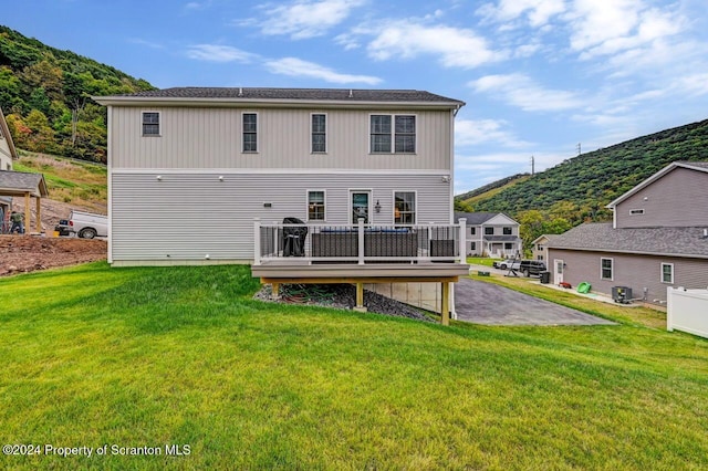 back of house with central AC unit, a deck with mountain view, and a lawn