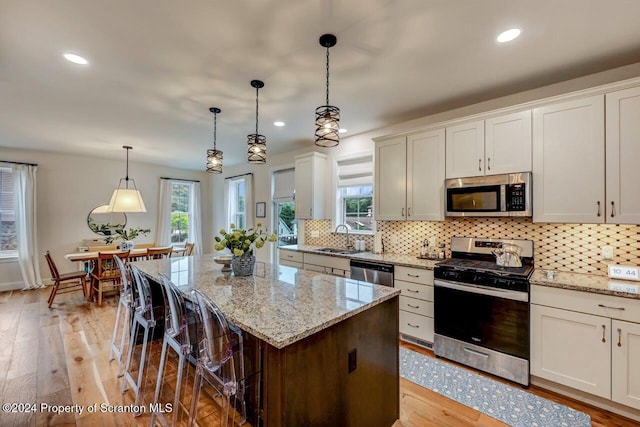 kitchen featuring white cabinets, stainless steel appliances, a kitchen island, and hanging light fixtures