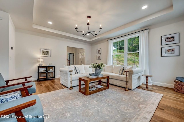 living room featuring a raised ceiling, light hardwood / wood-style floors, and an inviting chandelier