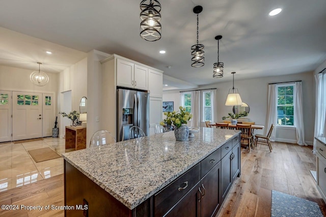 kitchen featuring stainless steel refrigerator with ice dispenser, dark brown cabinetry, pendant lighting, white cabinets, and a center island