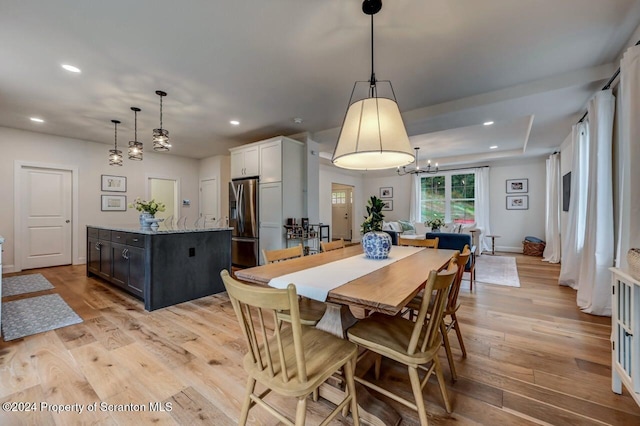 dining space featuring a tray ceiling, an inviting chandelier, and light wood-type flooring