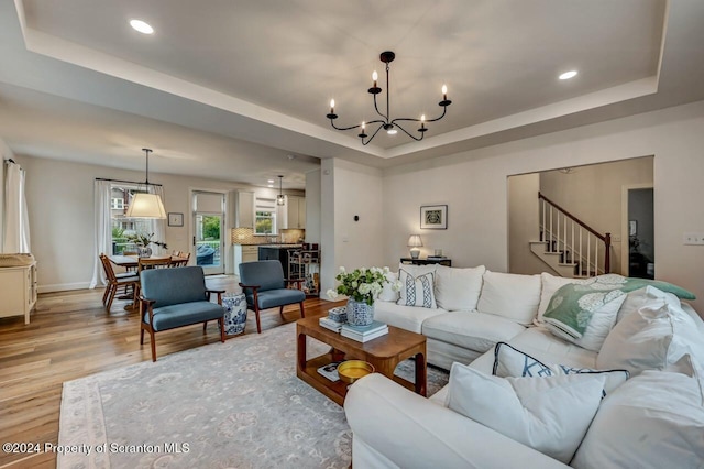 living room with a raised ceiling, light wood-type flooring, and a chandelier