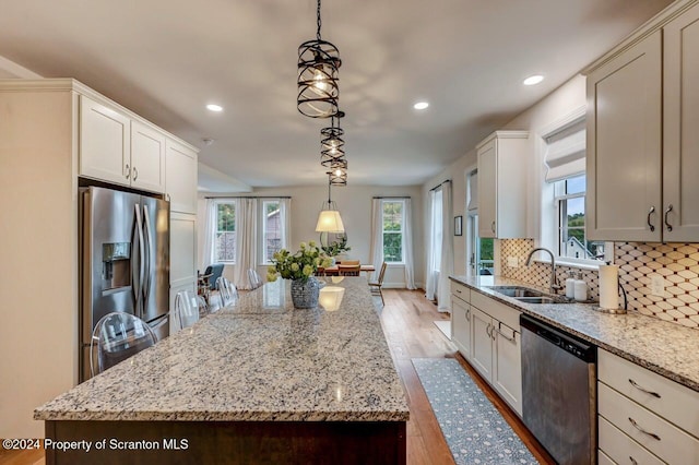 kitchen featuring pendant lighting, sink, appliances with stainless steel finishes, a kitchen island, and light stone counters