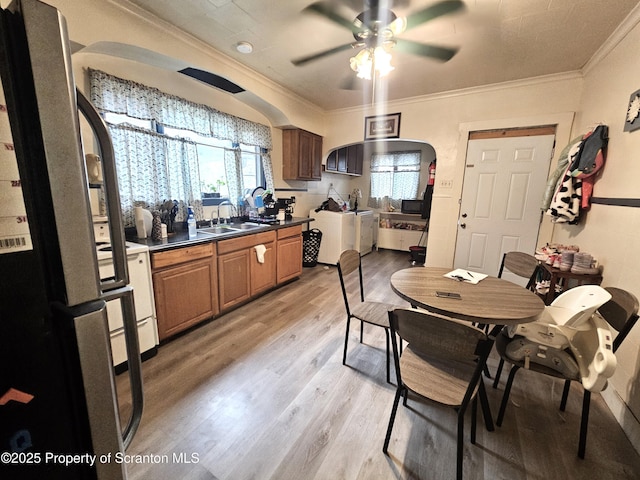 dining room with light wood finished floors, a ceiling fan, ornamental molding, and arched walkways