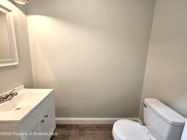 half bath featuring vanity, toilet, baseboards, and wood finished floors