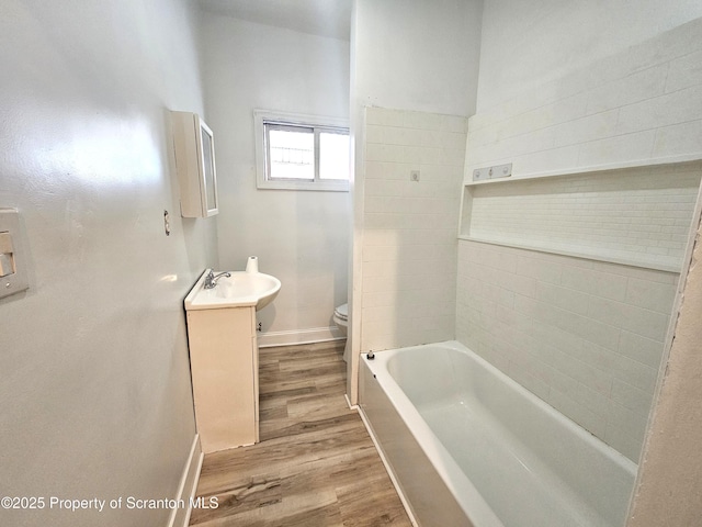 bathroom with toilet, wood finished floors, baseboards, a tub, and vanity