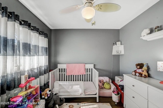 bedroom featuring a crib, ceiling fan, and wood finished floors