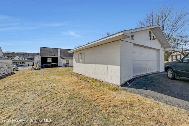 view of home's exterior with a yard, concrete block siding, an outdoor structure, and driveway