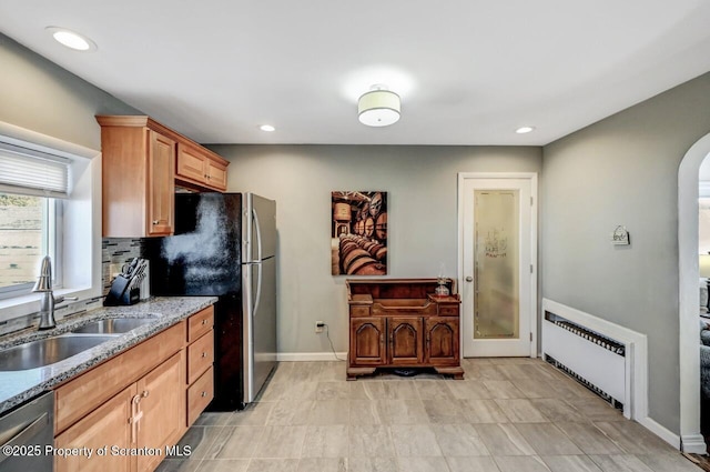 kitchen with a sink, stainless steel appliances, arched walkways, radiator, and light stone countertops