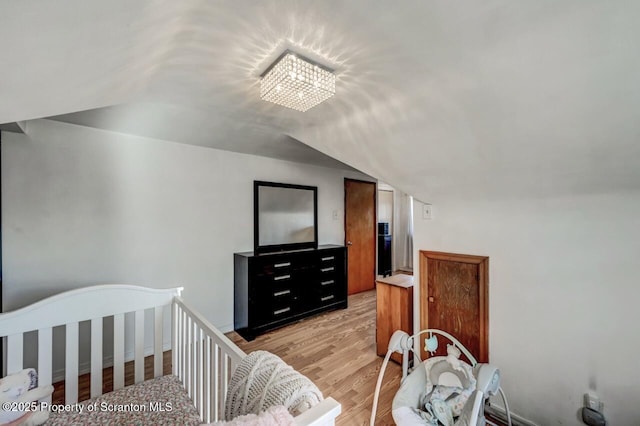 bedroom featuring light wood-style flooring, lofted ceiling, and an inviting chandelier