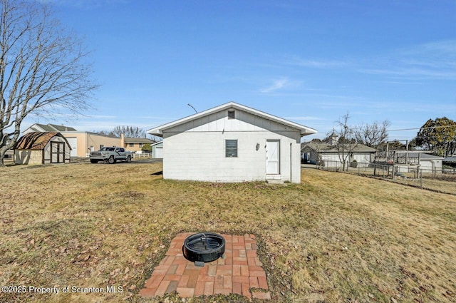 view of side of home with an outbuilding, fence, a yard, a fire pit, and a storage shed