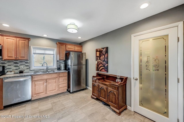 kitchen featuring light stone countertops, freestanding refrigerator, a sink, decorative backsplash, and dishwasher