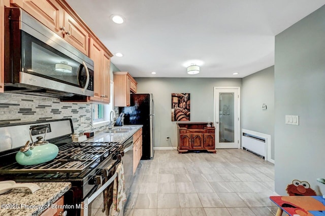 kitchen with radiator, light stone countertops, a sink, stainless steel appliances, and tasteful backsplash