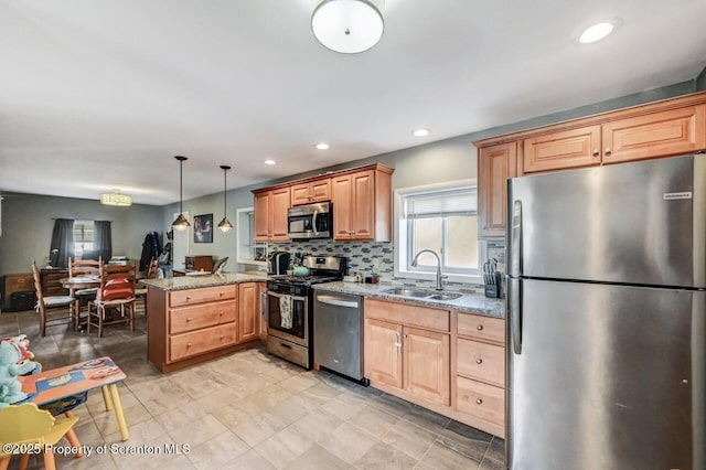 kitchen featuring a sink, light stone counters, tasteful backsplash, appliances with stainless steel finishes, and a peninsula