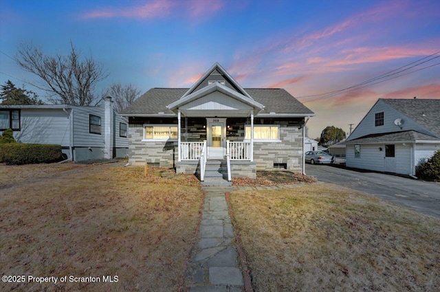 bungalow-style home with a porch, stone siding, and roof with shingles