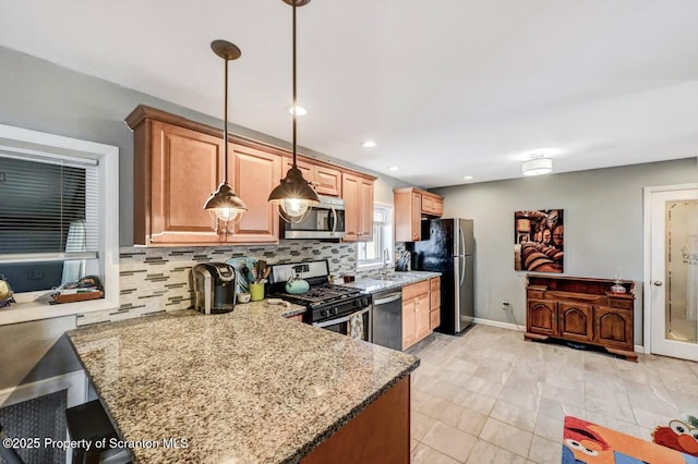 kitchen featuring light stone counters, a sink, hanging light fixtures, stainless steel appliances, and backsplash