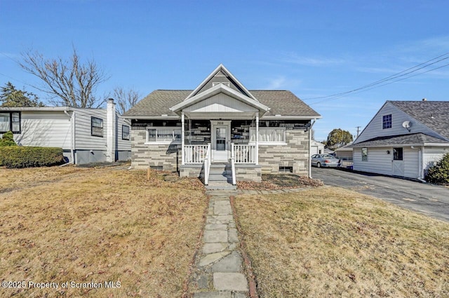 bungalow-style home with stone siding, covered porch, and roof with shingles