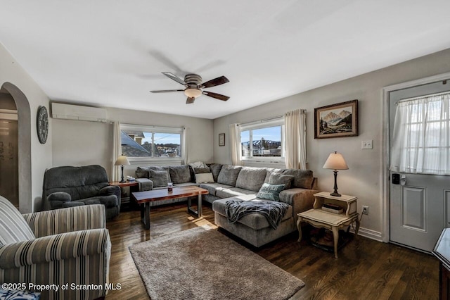 living room with dark wood-type flooring, a ceiling fan, arched walkways, and a wall mounted AC