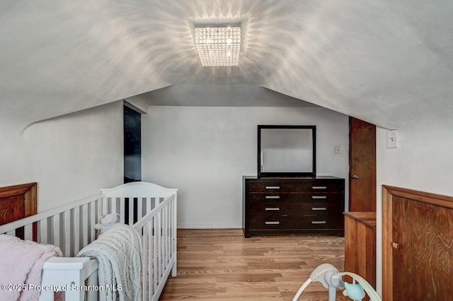 bedroom with an inviting chandelier, light wood-style flooring, and vaulted ceiling