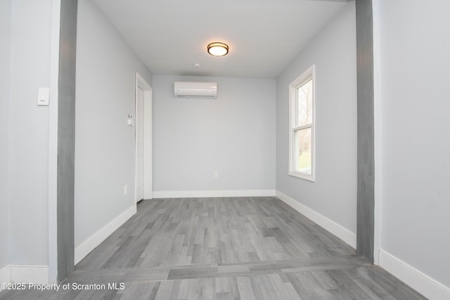 spare room with baseboards, wood finished floors, and a wall unit AC