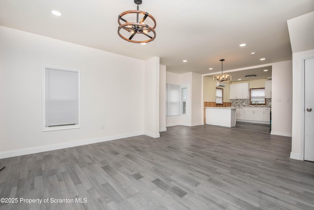 unfurnished living room with recessed lighting, wood finished floors, baseboards, and a notable chandelier