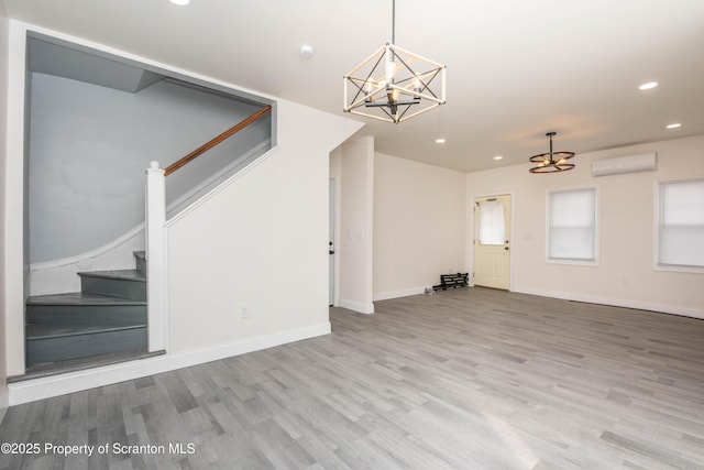 unfurnished living room with a wall mounted air conditioner, an inviting chandelier, wood finished floors, and stairs