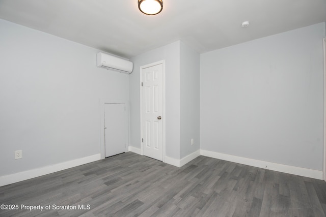 spare room featuring baseboards, wood finished floors, and a wall unit AC