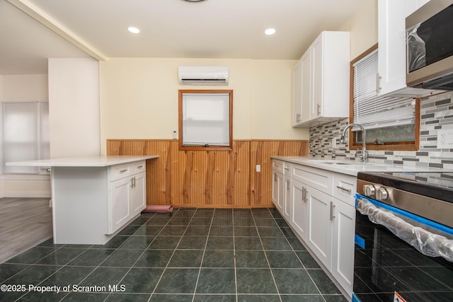 kitchen featuring a sink, a wall mounted AC, a wainscoted wall, white cabinets, and appliances with stainless steel finishes