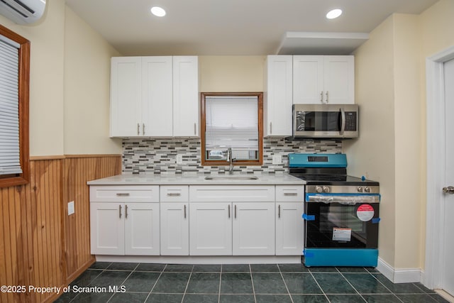 kitchen with an AC wall unit, appliances with stainless steel finishes, a sink, and white cabinets