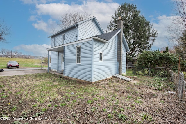 view of side of property featuring a lawn, a chimney, and fence