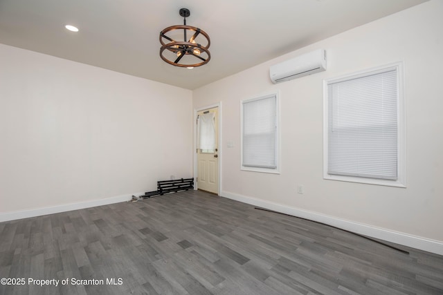 empty room featuring an AC wall unit, wood finished floors, baseboards, a notable chandelier, and recessed lighting