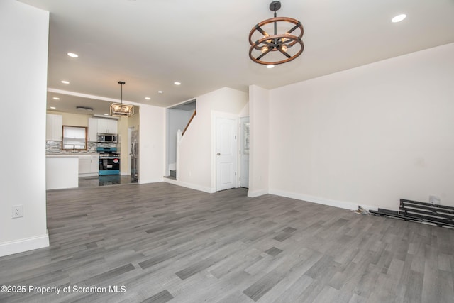 unfurnished living room featuring baseboards, a notable chandelier, wood finished floors, and recessed lighting