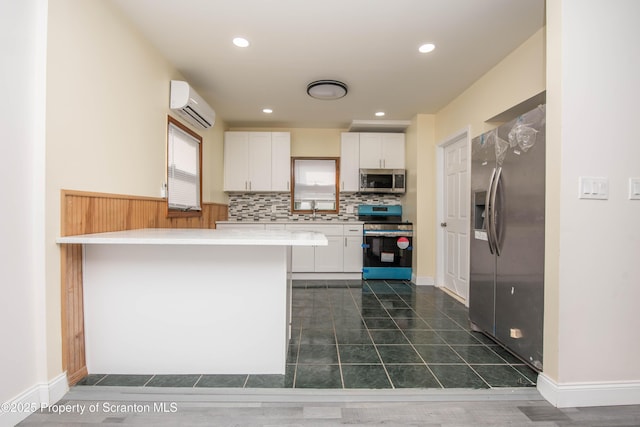 kitchen featuring a peninsula, a sink, a wall unit AC, white cabinetry, and appliances with stainless steel finishes