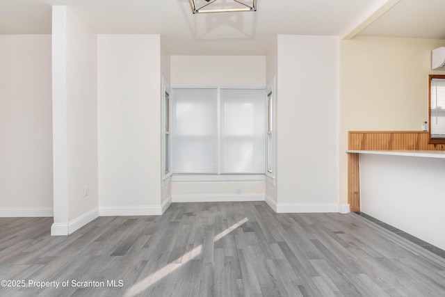 unfurnished dining area with baseboards, wood finished floors, an inviting chandelier, and a wall unit AC
