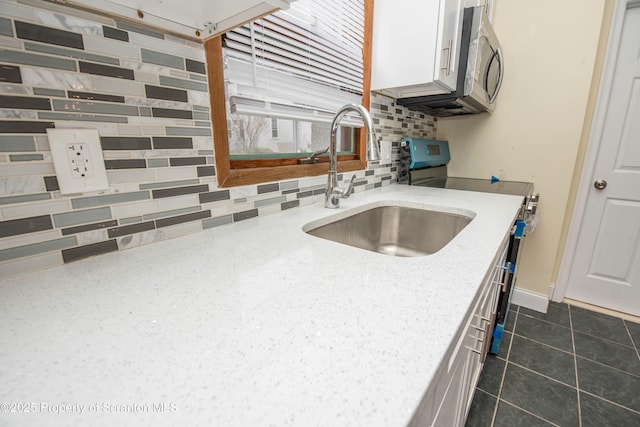 kitchen with light stone counters, backsplash, white cabinetry, and a sink
