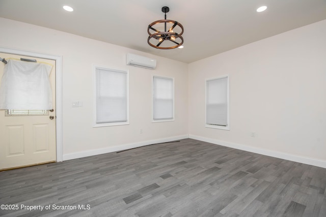 empty room with recessed lighting, wood finished floors, a wall unit AC, and an inviting chandelier