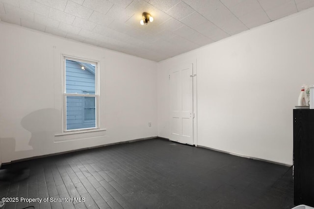 empty room featuring dark wood-style floors, baseboards, and ornamental molding