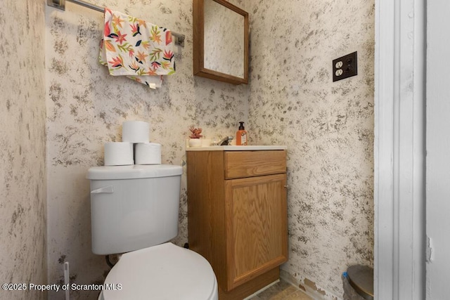 bathroom featuring toilet, wallpapered walls, and vanity