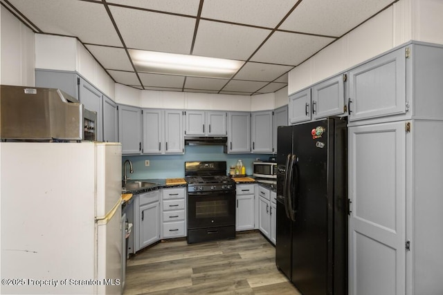 kitchen featuring under cabinet range hood, a sink, light wood-style floors, black appliances, and dark countertops