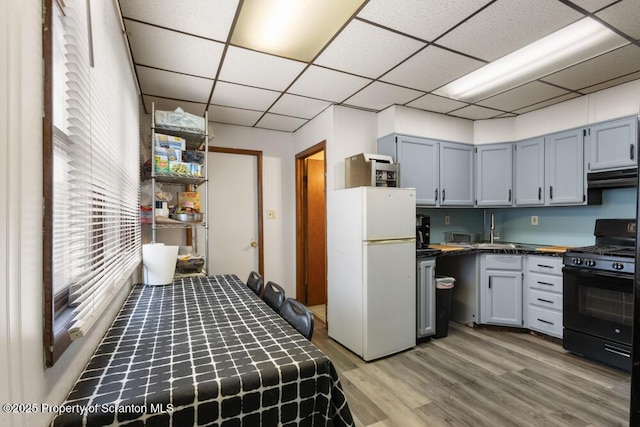 kitchen featuring a paneled ceiling, under cabinet range hood, black gas stove, freestanding refrigerator, and dark countertops