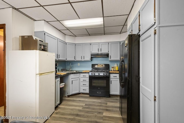 kitchen with under cabinet range hood, dark wood-type flooring, a sink, black appliances, and dark countertops