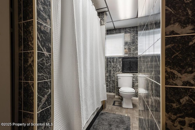 full bathroom featuring toilet, curtained shower, and tile walls