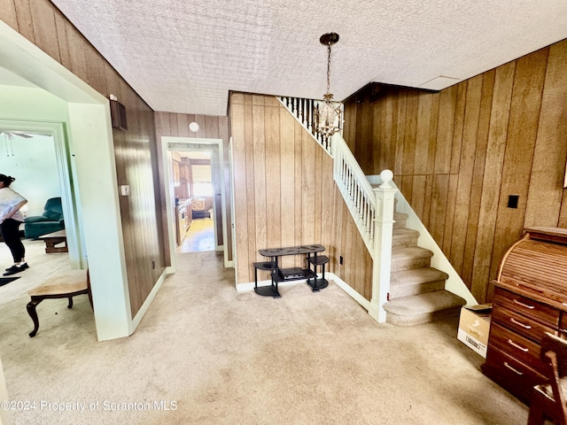 interior space with carpet flooring, wooden walls, a chandelier, and a textured ceiling