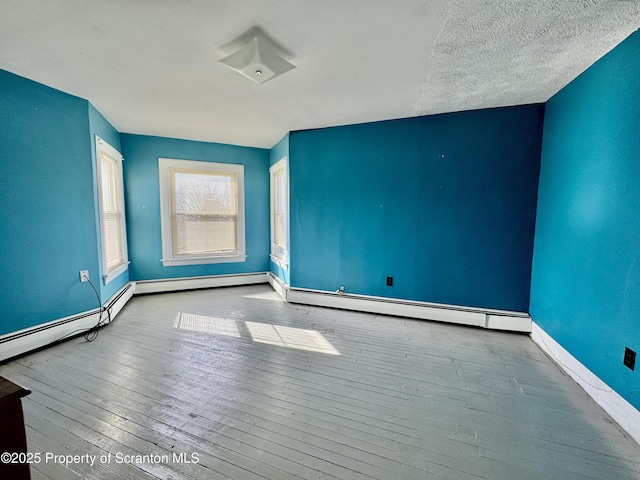 empty room with baseboards, a baseboard heating unit, and hardwood / wood-style floors