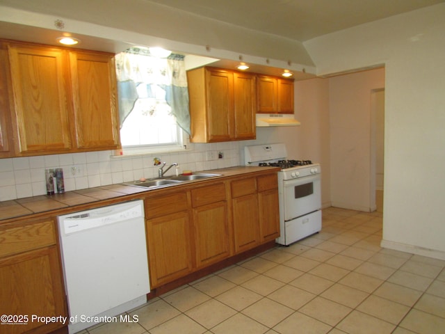 kitchen with white appliances, tile countertops, a sink, under cabinet range hood, and backsplash