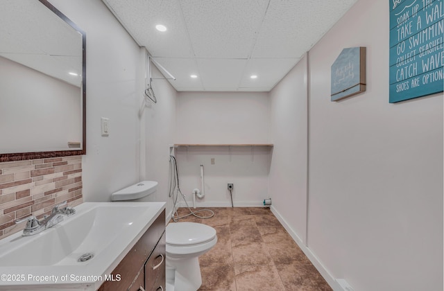 bathroom with a drop ceiling, vanity, decorative backsplash, and toilet